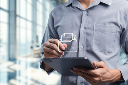 A businessman is checking a document on a tablet in a modern office. The image captures the focus on technology and productivity in a corporate workspace.の写真素材