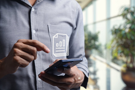 A businessman checks a document on his smartphone in a modern office environment. The focus is on technology and professional tasks, highlighting efficiency in the workspace.の写真素材