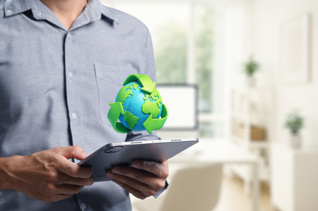 A person holds a tablet featuring a graphic of the Earth and recycling sign. This image promotes environmental consciousness and sustainability in a modern workspace.の写真素材