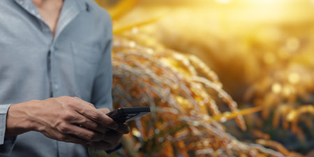 A farmer uses a smartphone in a field to enhance farm management. Technology plays a vital role in optimizing production and improving efficiency in agriculture.の写真素材