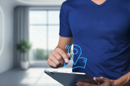 A person in a blue shirt interacts with a tablet device, highlighting a location pin icon. The modern indoor setting emphasizes technology and creativity.の写真素材