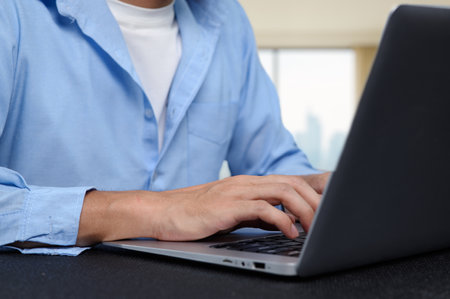 A person in a blue shirt focused on typing on a laptop in a bright modern workspace. This image captures the essence of productivity and contemporary work culture.の写真素材