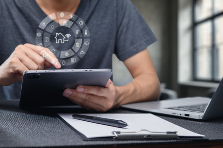 A person interacts with a tablet displaying smart home icons, symbolizing technology and connectivity in a modern workspace. The image captures innovation and digital communication.の写真素材