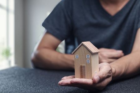 A person holds a small wooden house model in hand, symbolizing the exciting world of property trading and real estate investment opportunities.の写真素材