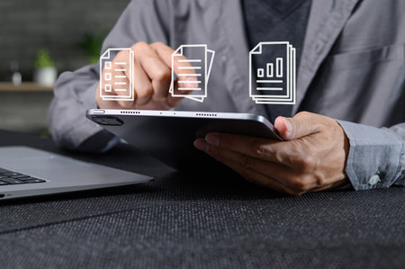 A person interacts with a tablet in a contemporary workspace, utilizing digital documents for efficient data management and enhancing productivity in a paperless environment.の写真素材