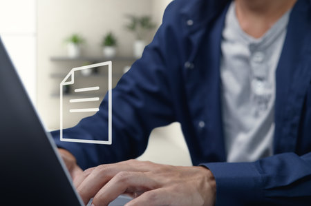 A focused individual engages with digital documents on a laptop, showcasing the modern shift towards technology for communication and efficiency in professional environments.の写真素材