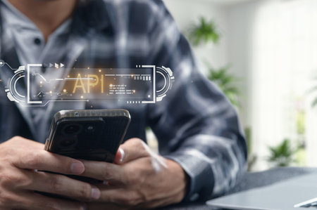 A person interacts with a smartphone displaying an API interface, symbolizing modern programming and technology in a bright workspace environment.の写真素材