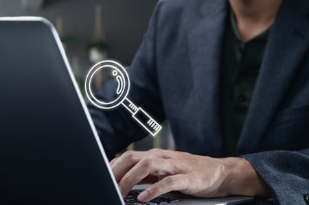 A professional user searches for information online using a laptop, featuring a glass icon to symbolize digital exploration and analysis of data in a modern workspace.の写真素材