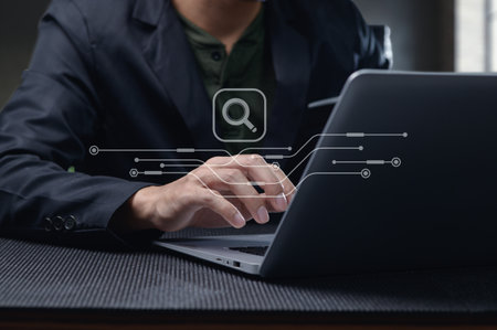 A person engages with a laptop, utilizing a search function symbolized by a glass icon. The image captures modern digital exploration in a professional workspace.の写真素材