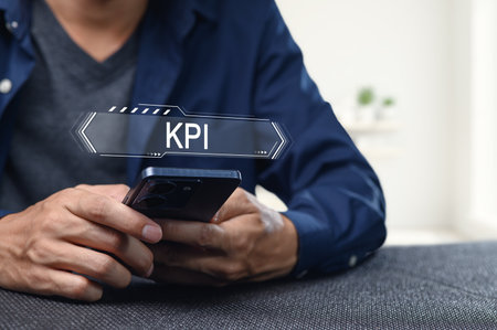 A close-up view of hands holding a smartphone displaying the term KPI, emphasizing the role of key performance indicators in modern business strategies and analytics.の写真素材