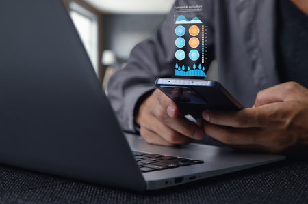 A person using a smartphone in a workspace with a laptop, showcasing innovative technology focused on sustainability solutions and digital integration.の写真素材