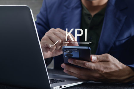 A businessman engages with his smartphone while analyzing key performance indicators on a laptop, representing modern business analytics and performance tracking.の写真素材
