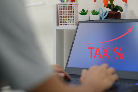 A close-up view of hands on a laptop depicting a tax increase concept with a growth arrow, illustrating financial trends and economic strategies.の写真素材