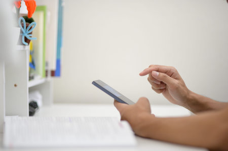 A close-up view of a person using a smartphone at a desk surrounded by papers, highlighting modern...