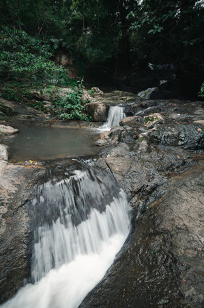 A breathtaking view of a tranquil waterfall flowing over rocky terrain, surrounded by lush greenery....