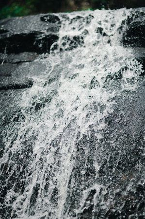 This stunning image captures a waterfall gracefully cascading over rugged rocks, showcasing the beauty of nature and the refreshing essence of flowing water in a serene setting.の写真素材