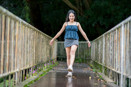 A cheerful young woman enjoys a leisurely walk along a serene forest pathway, surrounded by lush greenery and nature's beauty.の写真素材