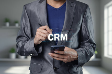 A businessman in a sleek suit engages with a mobile phone, showcasing CRM technology. The image represents modern relationship management and digital strategy.の写真素材