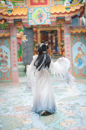 A graceful young woman wearing a beautiful Hanfu dress poses in a vibrant Chinese style setting, showcasing elegance and cultural heritage amidst stunning architectural details.の写真素材
