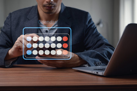 A businessman interacting with a digital calendar on his smartphone while seated at a desk with a...