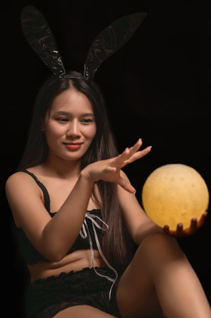 A cheerful young woman in a black bunny costume playfully holds a glowing sphere, creating a whimsical atmosphere perfect for Halloween or themed parties.の写真素材