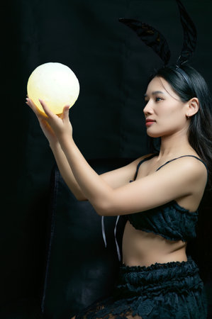 A stunning portrayal of a woman in a ghost bunny costume, holding a glowing sphere. The dark background enhances the mystical atmosphere, creating a captivating scene.の写真素材