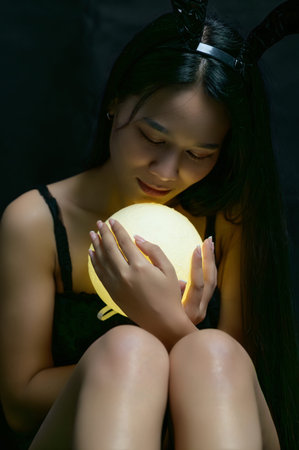 A serene portrait of a girl in a bunny costume, gently holding a glowing orb. The dark background...