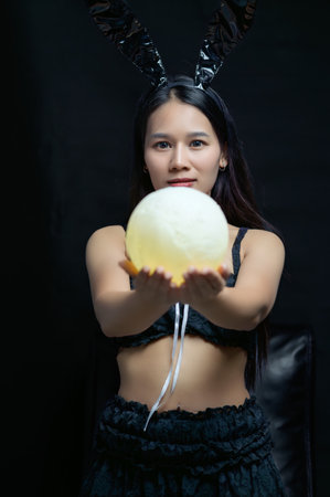 A woman models a playful bunny costume while holding a circular object. The dark background adds an air of mystery, creating a captivating and unique atmosphere.の写真素材