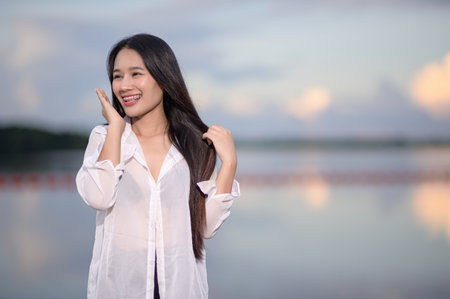 A happy young woman smiles joyfully outdoors, showcasing the beauty of nature. Her casual look and vibrant expression evoke feelings of positivity and relaxation.の写真素材