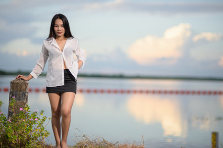 A young woman poses confidently by the water's edge, showcasing a casual outfit in a serene natural setting with stunning reflections and a peaceful atmosphere.の写真素材