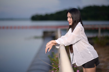 A serene young woman poses by the water's edge, embodying tranquility and beauty in nature during sunset, perfect for tourism and outdoor lifestyle themes.の写真素材