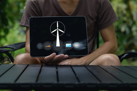 A person holds a tablet showcasing a wind turbine graphic that represents electricity production and renewable energy technology, highlighting sustainability.の写真素材