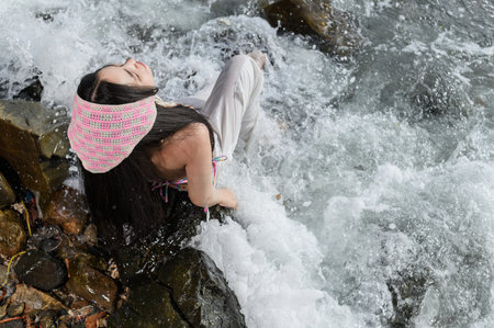 A woman enjoys the serene beach environment, sitting on rocks as waves splash around her, capturing the essence of freedom and relaxation at the ocean.の写真素材