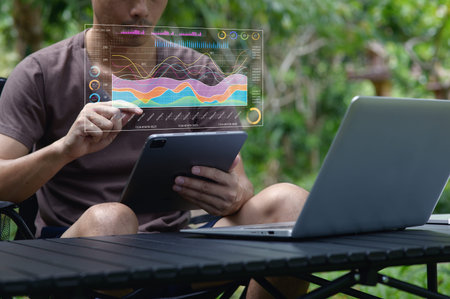 A man engages in data analysis using a tablet while seated outdoors with a laptop, showcasing modern...