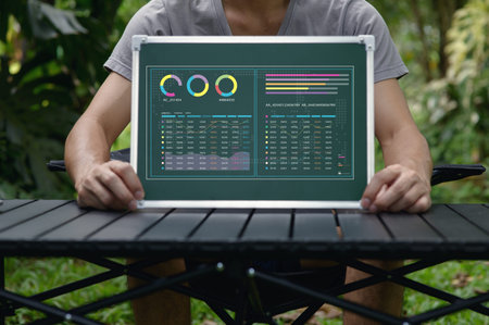 A person sits outdoors, holding a presentation board filled with various data charts and statistics....