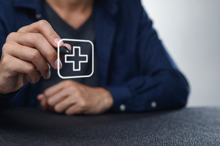 A person's hand holds a transparent health icon featuring a plus sign, symbolizing care and support in healthcare settings, illustrating modern health services.の写真素材