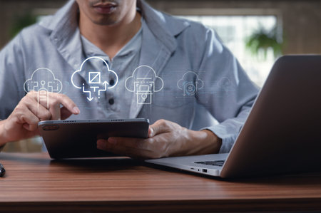 A man engages with a tablet in a modern workspace, illustrating cloud computing and file transfer...