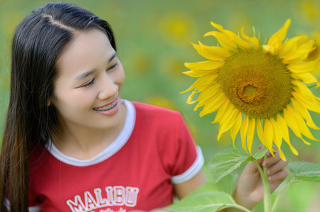 A joyful woman interacts with a vibrant sunflower in a sunny field, capturing the essence of nature's beauty and the warmth of summer joy.の写真素材