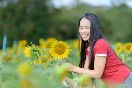 A young woman smiles joyfully while standing amidst a vibrant sunflower field. The bright sunny day enhances the cheerful atmosphere, showcasing nature's beauty.の写真素材