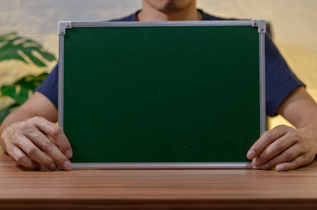 A person is holding a blank green board in a modern office setting, perfect for presentations or creative displays. The tranquil atmosphere enhances focus.の写真素材
