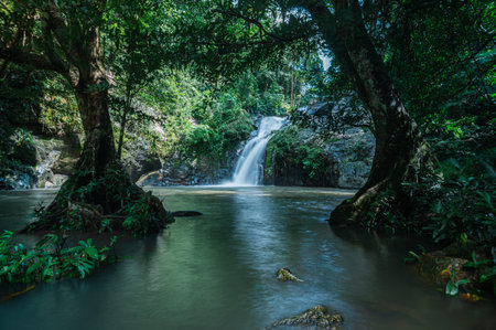 A stunning waterfall cascades through a vibrant green forest, creating a tranquil scene. Sunlight...