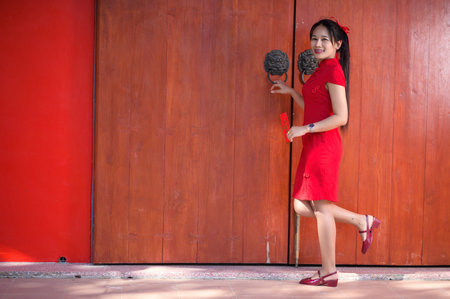 A joyful woman celebrates the New Year wearing a bright red dress, sophisticated accessories, posing elegantly against a vibrant red backdrop filled with festive spirit.の写真素材