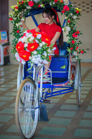 A joyful woman in a red dress rides a decorated cycle rickshaw, surrounded by colorful flowers and...