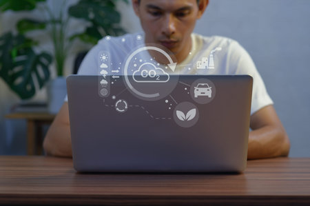 A young man engaged in work on his laptop, featuring environmental icons representing sustainability...