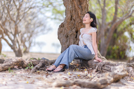 A serene woman enjoys a moment of relaxation by a tree on Koh Si Chang beach in Thailand. The sunlight enhances the tranquil atmosphere, perfect for vacation.の写真素材