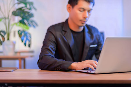 A young professional man focused on his laptop in a modern office setting, showcasing technology and...