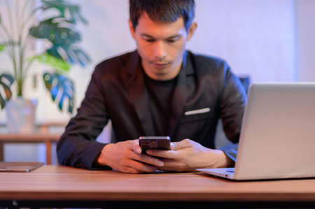 A young man engages with his smartphone while seated at a modern home office desk, featuring a...
