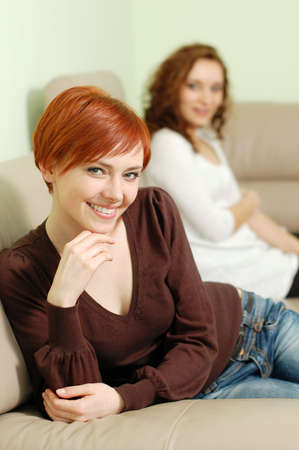 Closeup of a woman smiling delicately with another woman sitting in the background.の写真素材
