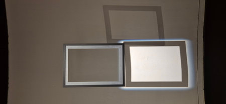 Two frames on a wall in a room with a lighted window