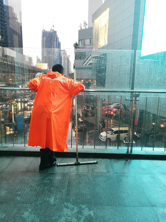 A man in orange raincoat and black boots with  equipment cleaning leaning on balconyのeditorial素材